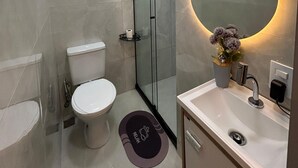 Une salle de bain moderne avec une douche en verre, des toilettes blanches, un lavabo avec un miroir et une petite plante en pot.