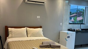 Une chambre avec un lit, un climatiseur, une fenêtre et un coin cuisine.