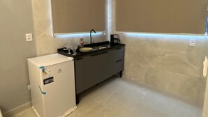 Une cuisine de taille réduite, dotée d’un réfrigérateur encastré, d’un plan de travail foncé et d’une fenêtre située au-dessus de l’évier.