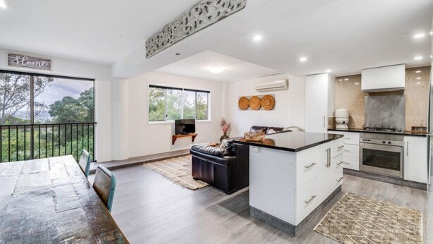 A modern kitchen with white cabinetry, a central island, and a dining area with a wooden table and chairs. - 3 Bedrooms Vista Point Sanctuary (Burleigh Heads)