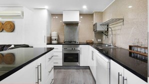 A modern kitchen with white cabinets, a black countertop, stainless steel appliances, and a built-in oven. - 3 Bedrooms Vista Point Sanctuary (Burleigh Heads)