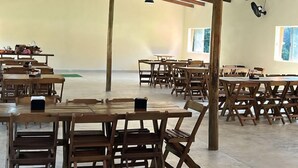 Un vaste espace intérieur doté de hauts plafonds et de poutres en bois, aménagé avec de nombreuses tables et chaises, idéal pour les repas ou les réunions.