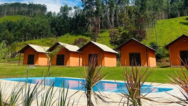 Un espace piscine avec quatre cabanes orange, entouré de verdure et de collines.