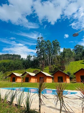 A pool area with four orange cabins, surrounded by greenery and hills. - Pousada rural família Nicolin  (Paraibuna)