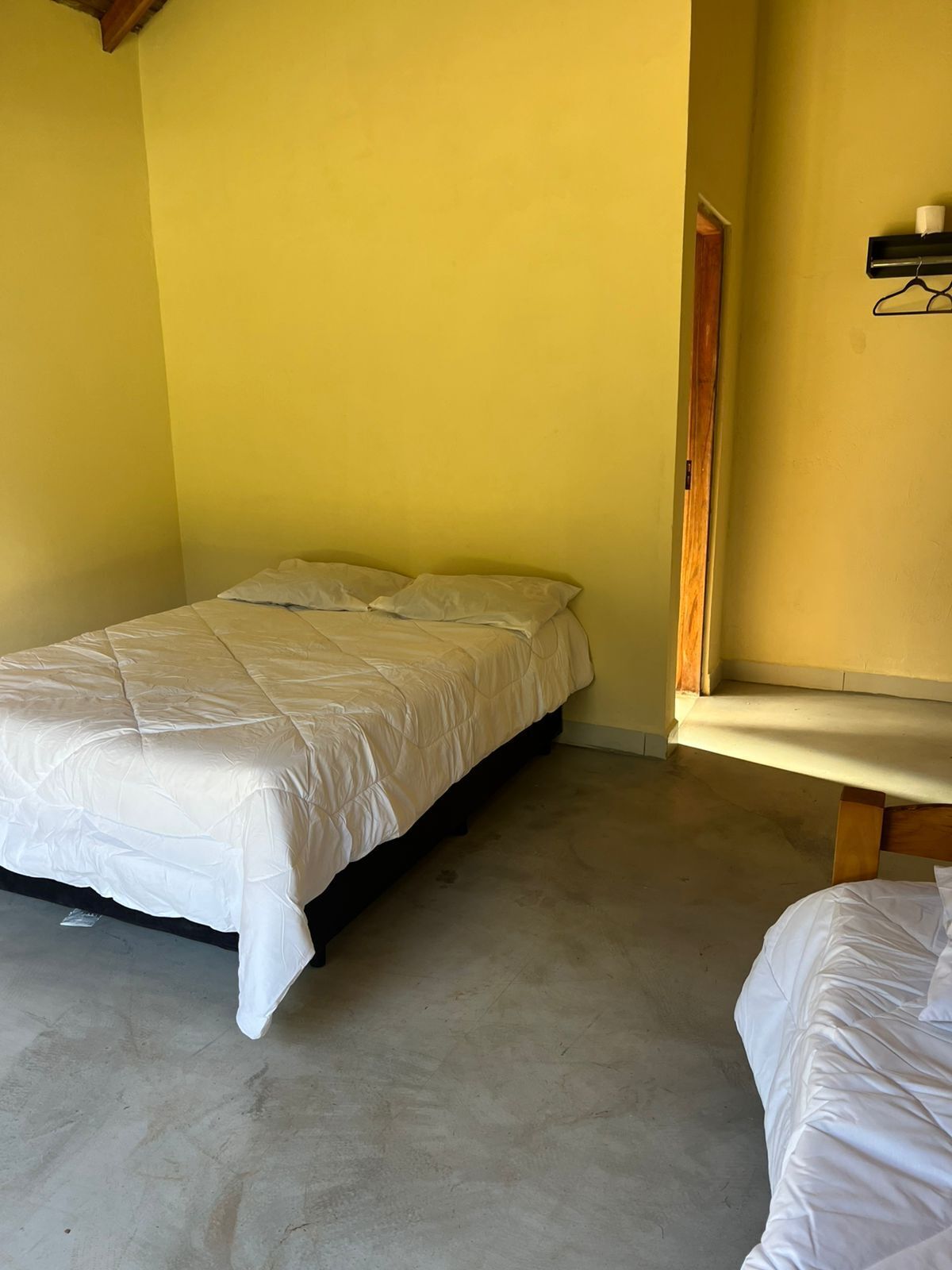 Una habitación con una cama, un banco y una estantería de pared con una taza y un perchero.