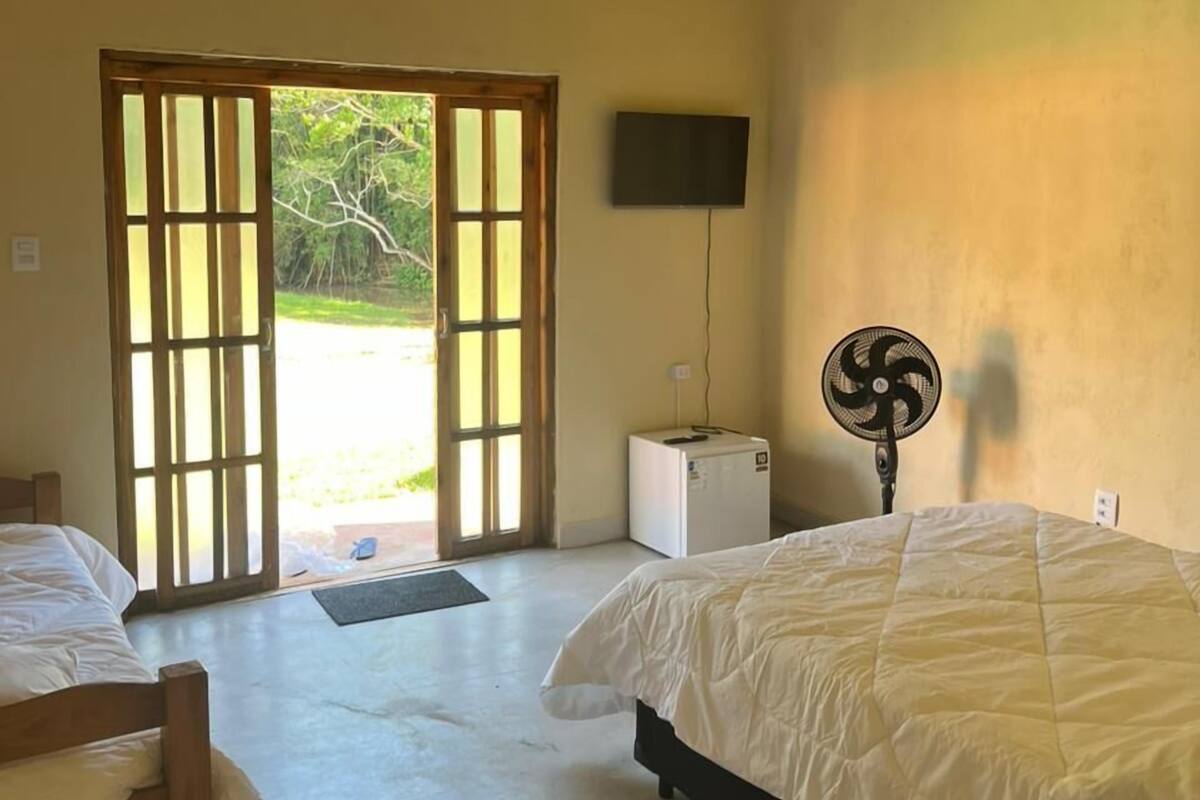 A room with two beds, a television, a fan, and a door leading outside.