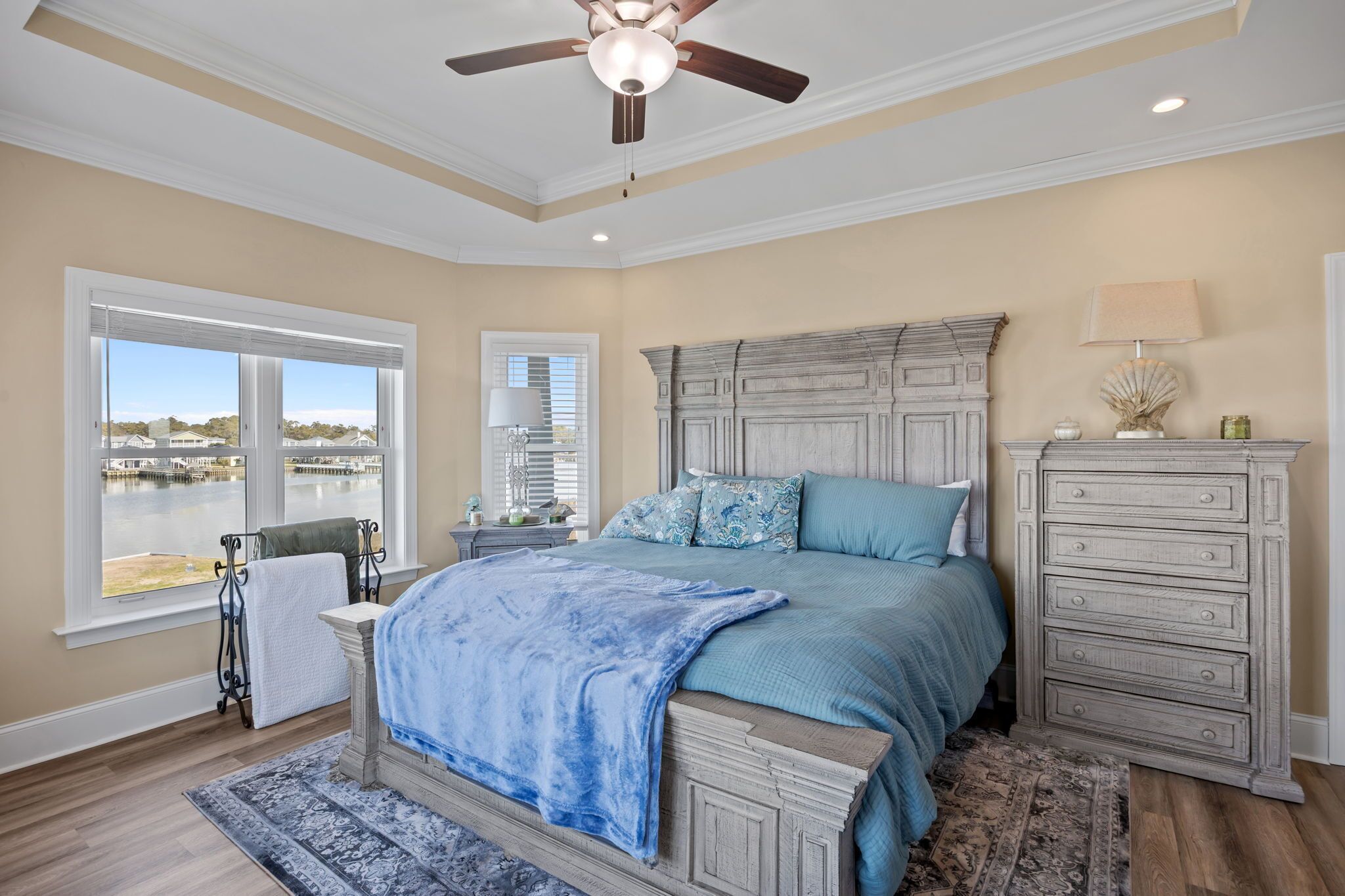 A bedroom with a large bed, a dresser, a nightstand, and a window with a view of a body of water.