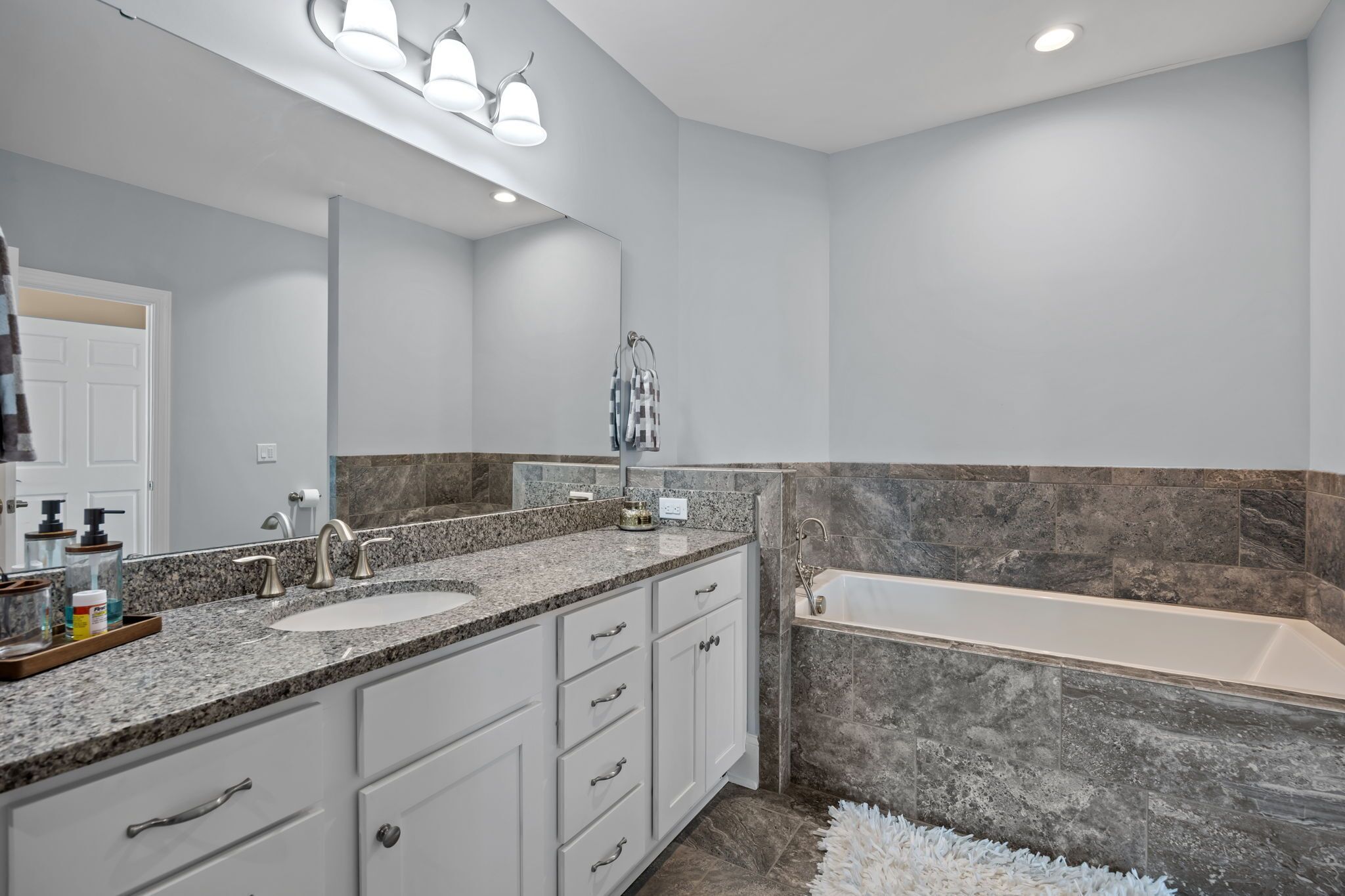 A modern bathroom with a double sink vanity, a bathtub, and a large mirror.