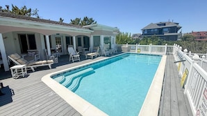 Une piscine dotée d’une terrasse en bois, de chaises longues et d’un espace couvert agrémenté d’une rambarde.