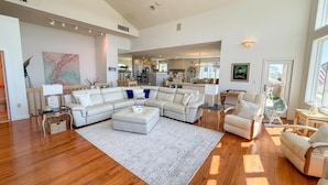 A spacious living room with a large sectional sofa, a coffee table, and a rug. There is a kitchen area visible in the background. - Beach Front. Water Views. Inground Pool. (Cape May)