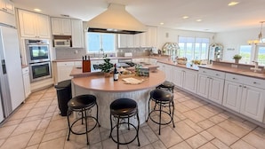 A modern kitchen with a central island, bar stools, and a view of the outdoors. - Beach Front. Water Views. Inground Pool. (Cape May)