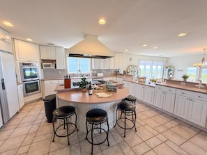 A modern kitchen with a central island, bar stools, and a view of the outdoors.