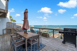 A wooden deck with a table and chairs, a barbecue grill, and a view of the ocean.