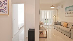 Un salon moderne avec un canapé, une table basse et un meuble pour la télévision. Une porte donne accès à un balcon d’où l’on peut admirer le paysage extérieur.