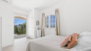 Ein Schlafzimmer mit Bett, Vorhängen, einem Fenster und Blick auf Grün.