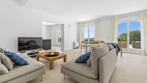 Ein modernes Wohnzimmer mit einem Flachbildfernseher, zwei Sofas, einem Couchtisch und einem Essbereich mit Tisch und Stühlen.