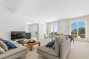 Ein modernes Wohnzimmer mit einem Flachbildfernseher, zwei Sofas, einem Couchtisch und einem Essbereich mit Tisch und Stühlen.