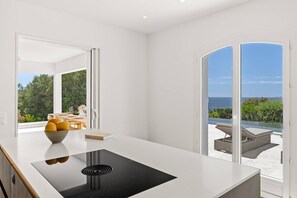 A modern kitchen with a large island, a bowl of fruit, and a view of a patio with outdoor furniture. - DAVIA - 5 bedrooms, 1 flat, panoramic sea view, swimming poo (PORTICCIO)