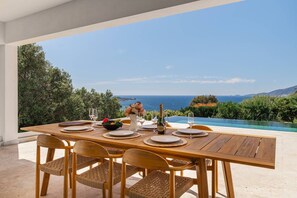 Mesa de refeições ao ar livre com vista para o mar e colinas.