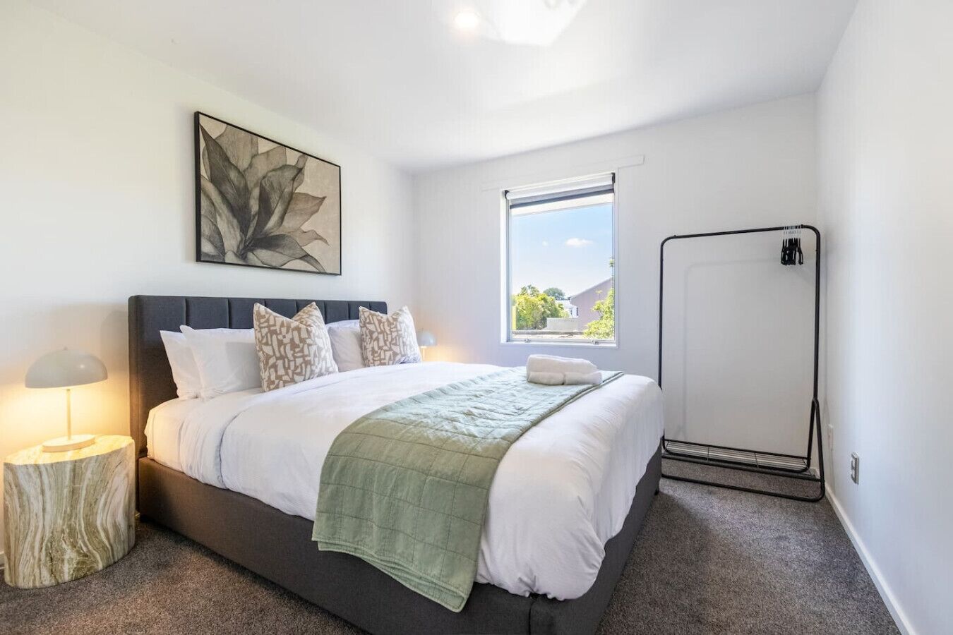 Quarto moderno com uma cama grande, uma janela com vista, uma mesa de cabeceira com abajur e um radiador.
