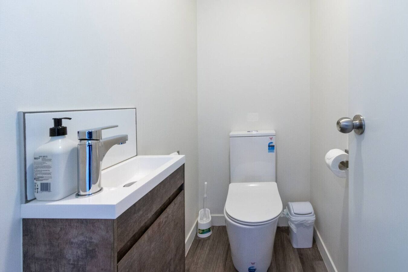 A modern bathroom with a white sink, a toilet, and a trash bin.