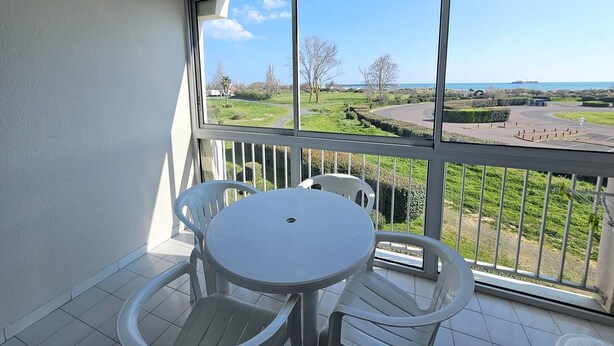 Een balkon met een witte tafel en stoelen, met uitzicht op een groen landschap en een weg.