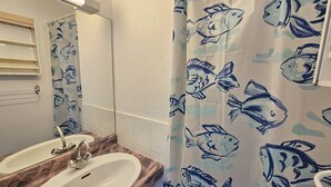 Een badkamer met twee wastafels, een spiegel en een douchegordijn met een vispatroon.