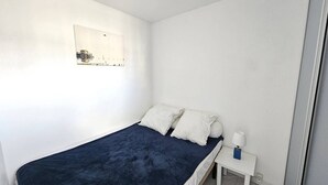 Een kleine, eenvoudige slaapkamer met een enkel bed, een nachtkastje en een wandlamp.