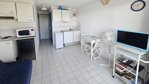 Een compacte keuken met witte kastjes, een magnetron, een kleine koelkast en een eethoek met een tafel en stoelen.