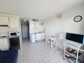 A compact kitchen with white cabinets, a microwave, a small refrigerator, and a dining area with a table and chairs. - CAP D'AGDE - Plage Richelieu / Réf 278 (CAP D'AGDE)