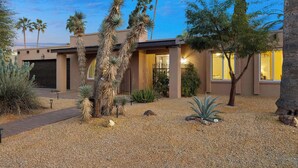 Une maison moderne dotée d’un jardin de style désertique, agrémenté de cactus et de palmiers, avec une allée et un garage.