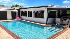 A swimming pool with a tiled deck, a covered seating area, and a building with large windows. - Versace Vibes Retreat, Pool Sauna Near Hard Rock (Hollywood)