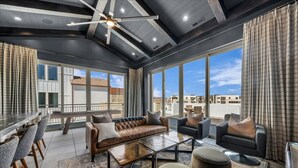 A spacious living area with a high ceiling, large windows, and a modern ceiling fan.