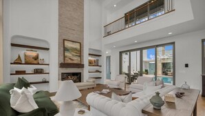 A spacious living room with a fireplace, multiple seating areas, and a balcony overlooking a pool.