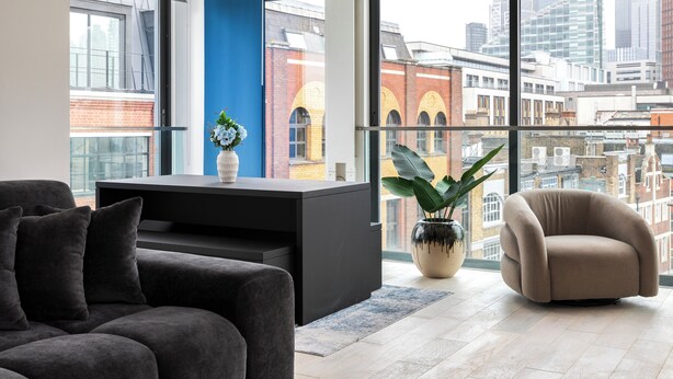 Ein modernes Wohnzimmer mit einer Couch, einem Sessel, einem schwarzen Konsolentisch und einem großen Fenster mit Blick auf die Stadt.