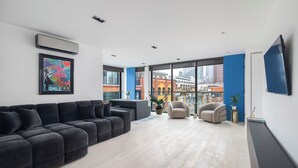 Ein modernes Wohnzimmer mit einer Eckcouch, einem kleinen runden Tisch und einem großen Fenster mit Blick auf die Stadt.