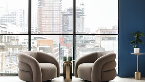 Ein modernes Zimmer mit zwei Sesseln, die auf ein großes Fenster mit Blick auf eine Stadtlandschaft ausgerichtet sind.