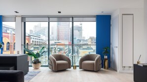 Ein modernes Wohnzimmer mit zwei Sesseln, einem Couchtisch und einem großen Fenster mit Blick auf die Stadt.