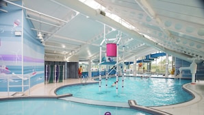 Ein Hallenbad mit farbig gestalteter Decke, einer Wasserrutsche und einem Rettungsschwimmerstand.