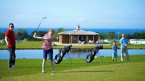 Ein Golfplatz mit Teich, Kiosk und freiem Blick auf den Ozean.