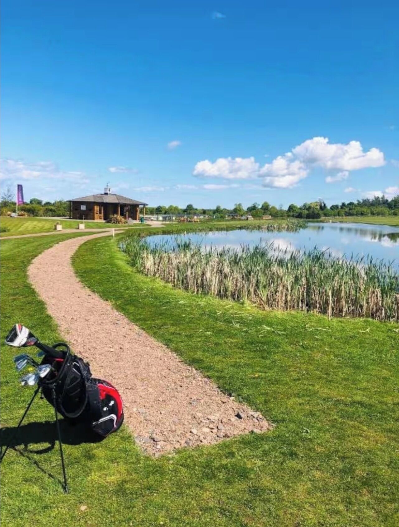 Un parcours de golf avec un étang, un club-house et un sentier menant à l’étang.