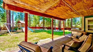 Un espace extérieur abrité, doté d’un plancher en bois, de sièges et offrant une vue sur un jardin avec une balançoire et des arbres.
