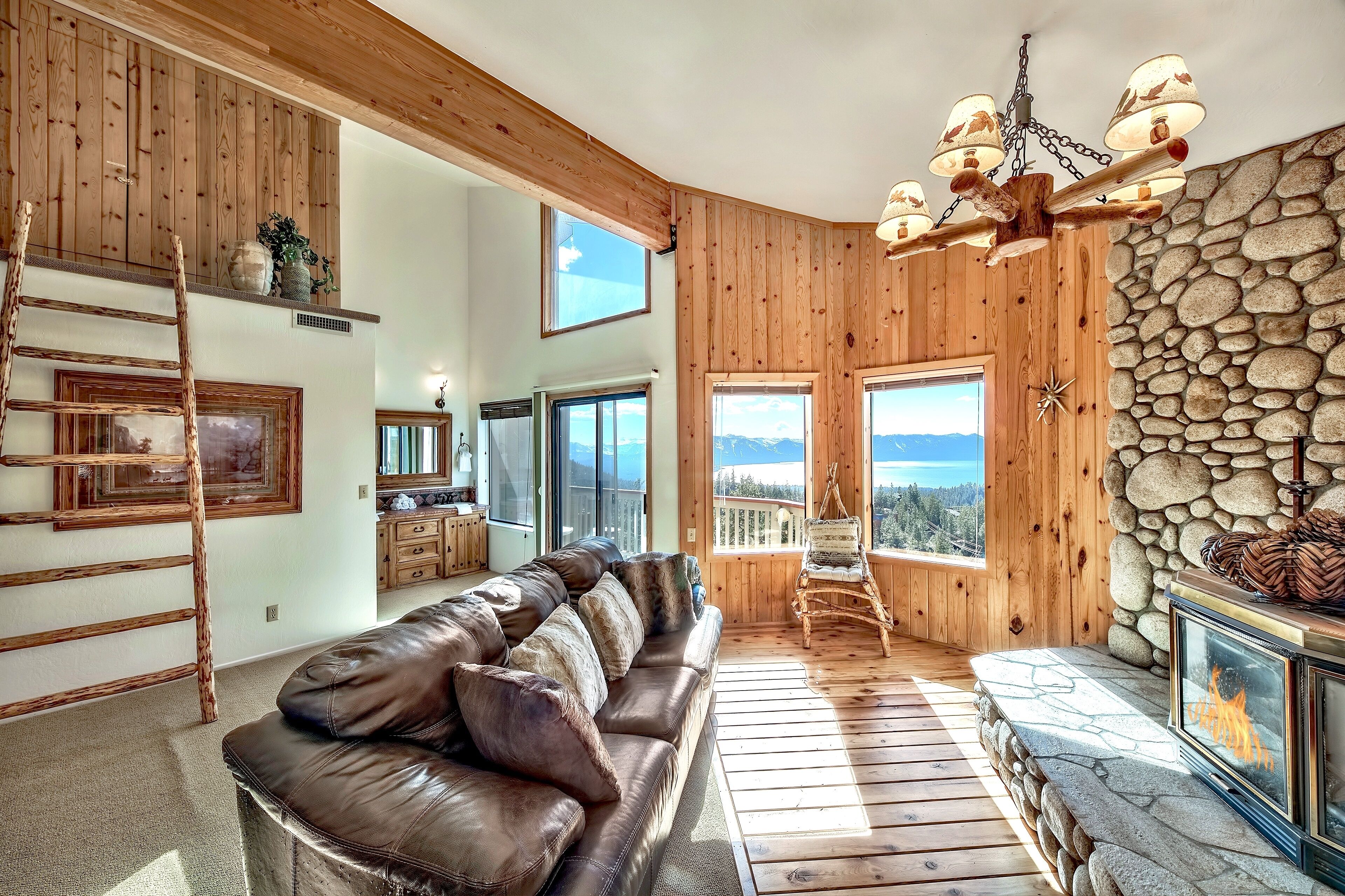 Un intérieur en bois avec un canapé en cuir, une cheminée en pierre et une vue dégagée grâce à de grandes fenêtres.