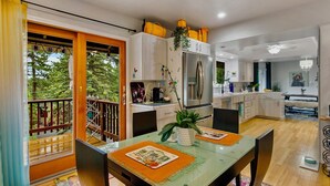 A modern kitchen with white cabinets, a stainless steel refrigerator, and a dining area with a glass table and chairs. - LX35  The Wolf Round Hill Retreat in the heart of Lake Tahoe (Zephyr Cove)