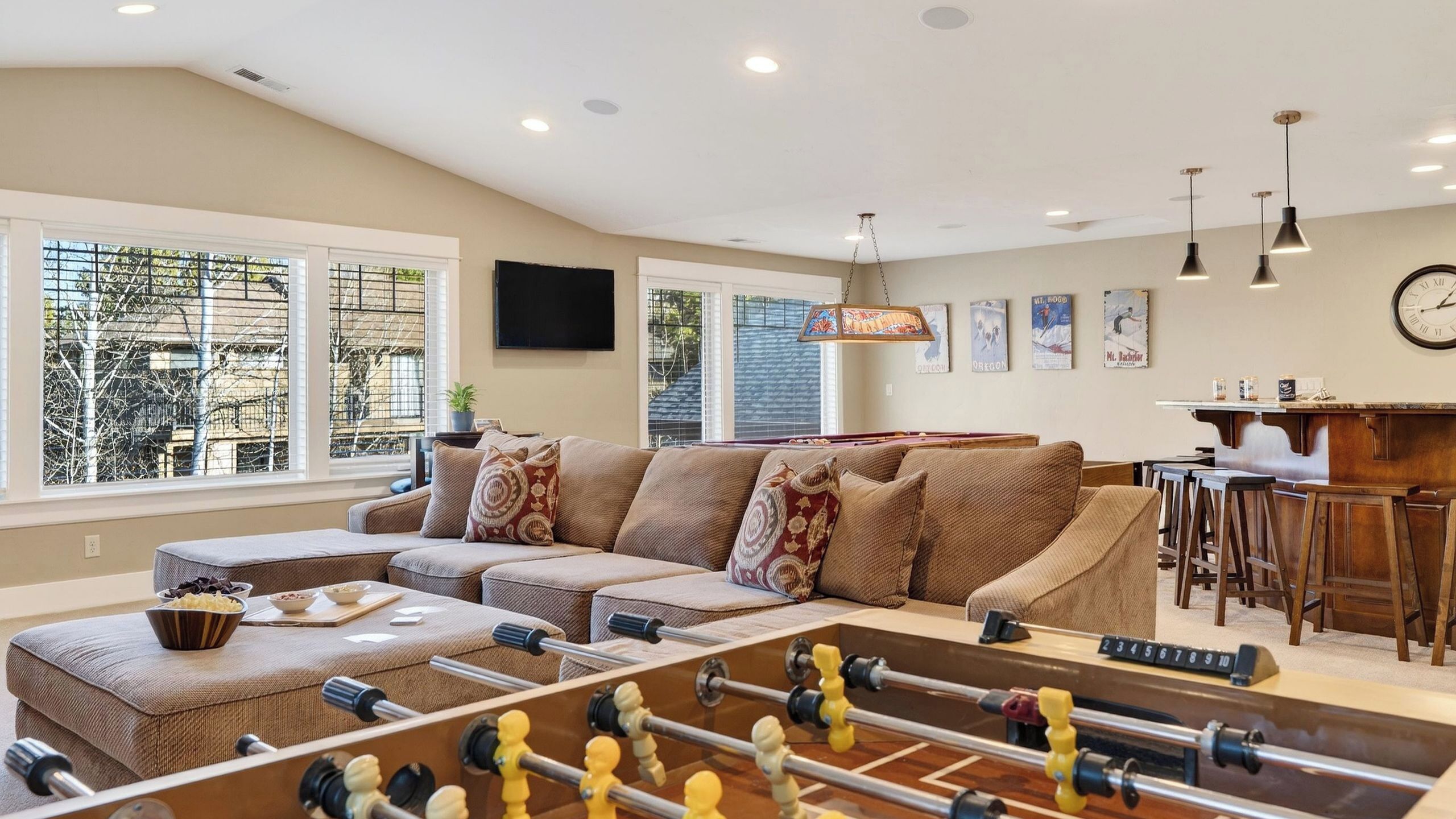 A living room with a foosball table, a sofa, a coffee table, and a kitchen area with a bar.