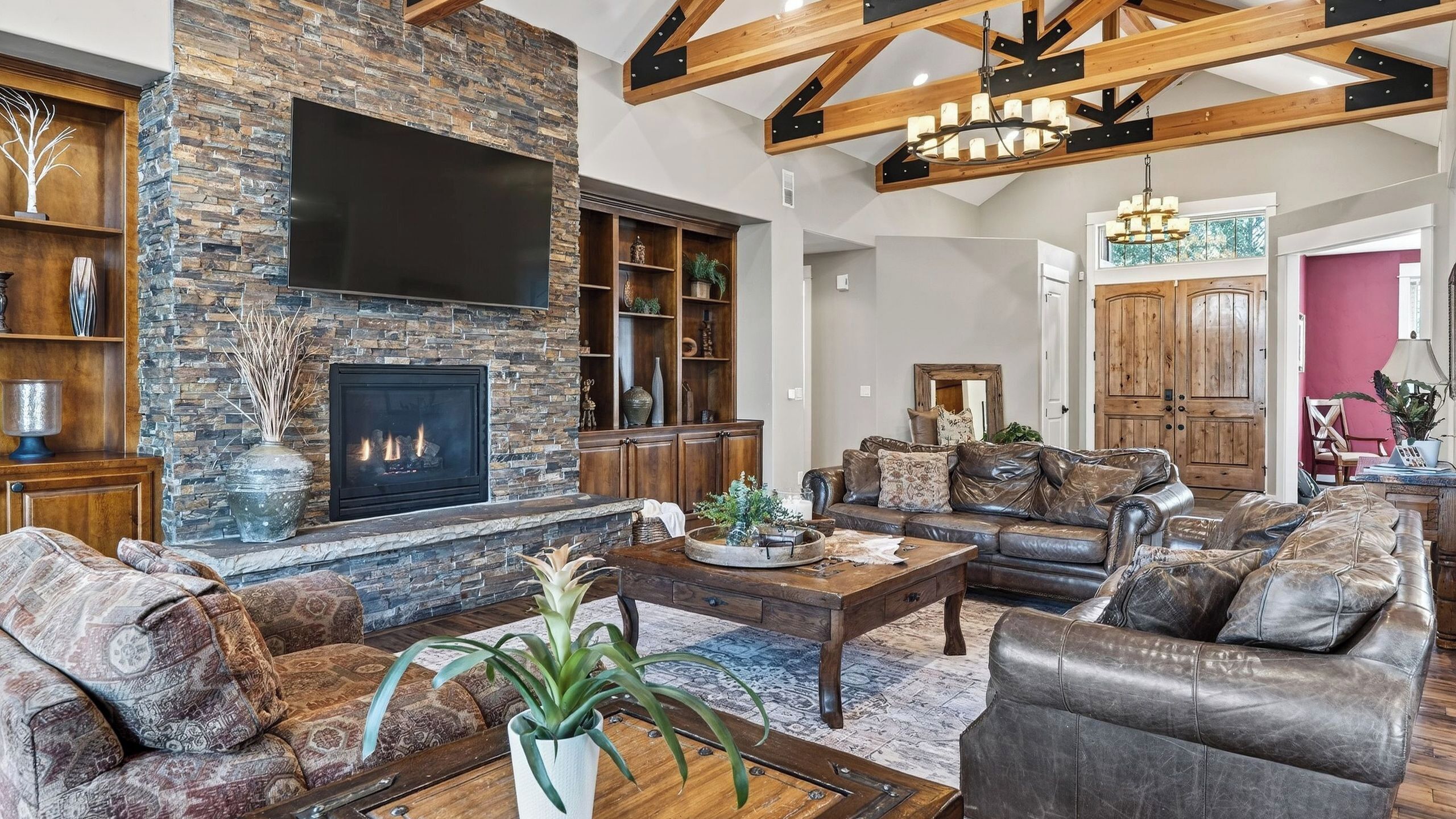Una sala de estar amplia con chimenea de piedra, sofás de cuero y un televisor de pantalla plana grande.
