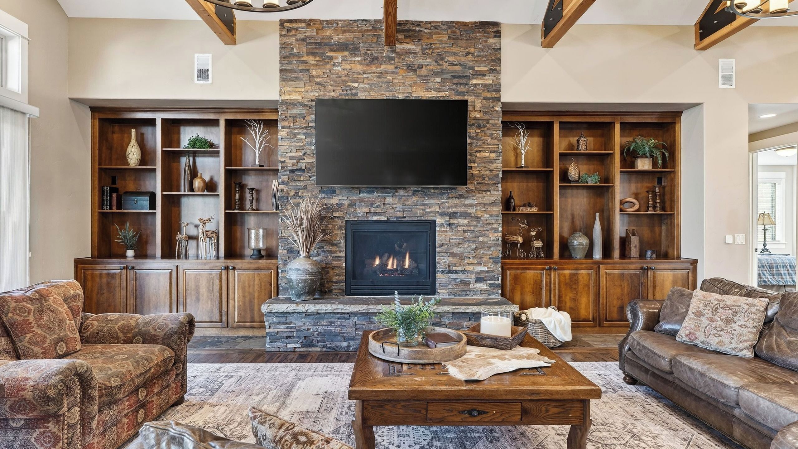 A living room with a stone fireplace, wooden shelves, and a large flat-screen TV.