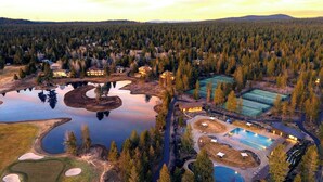 Luchtbeeld van een resort met meerdere tennisbanen, een zwembad en een meer, omgeven door dicht bos.