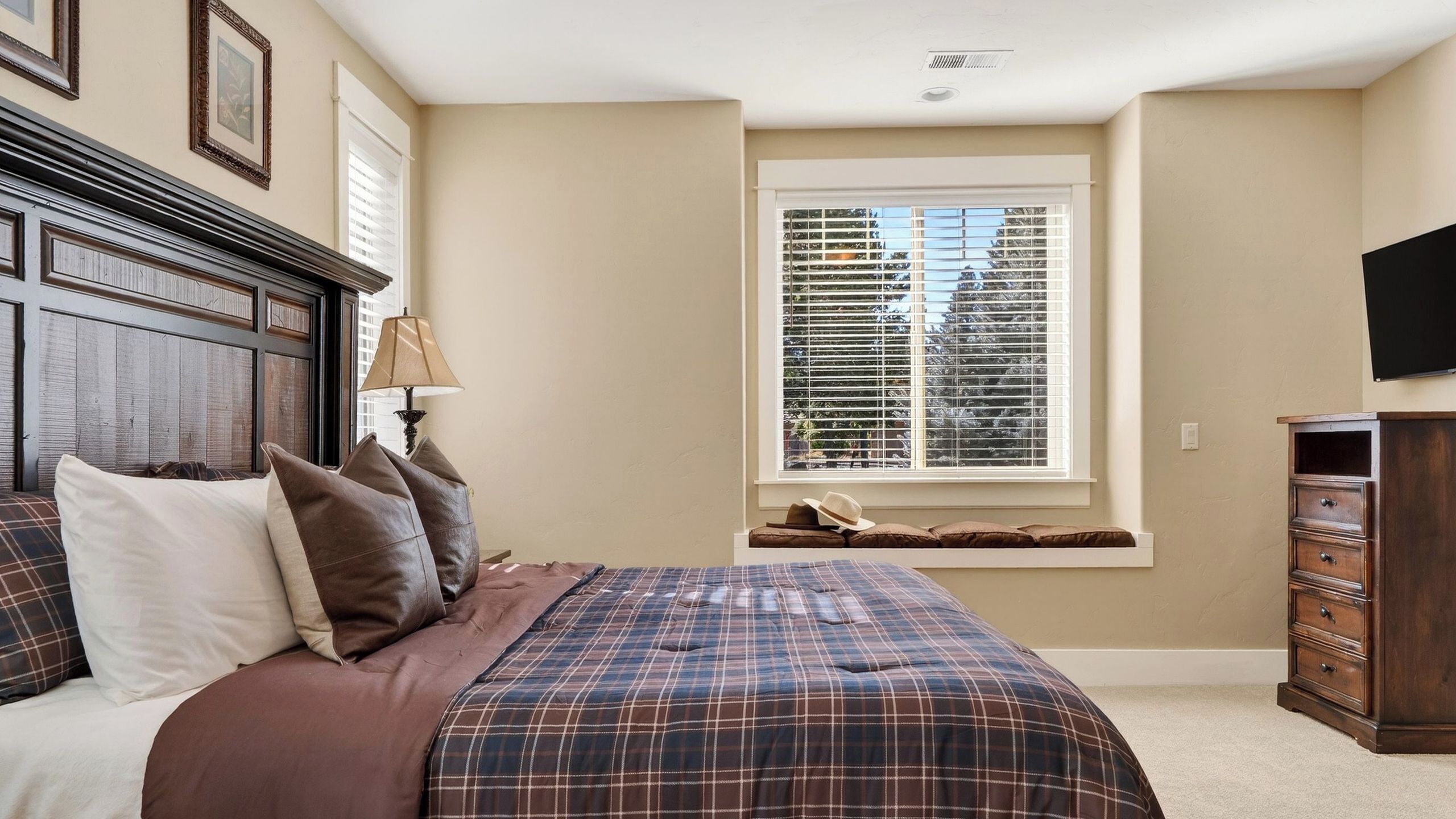 A bedroom with a bed, a window with blinds, a lamp, and a dresser.