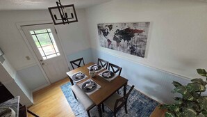 Un comedor con una mesa de madera dispuesta para cuatro, un mapa del mundo en la pared y una planta grande en la esquina.